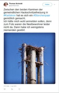 Ein Storchenpaar hat sich auf den Schornsteinen der Hackschnitzelheizung in Karlskron niedergelassen. Das Foto zeigt das beeindruckende Nest zwischen den Schornsteinen vor einem klaren blauen Himmel. Die Storchenbewohner waren jedoch leider nicht zu sehen, als das Foto aufgenommen wurde.
